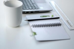 A mug, laptop, notebook, and ruler placed on a white desk