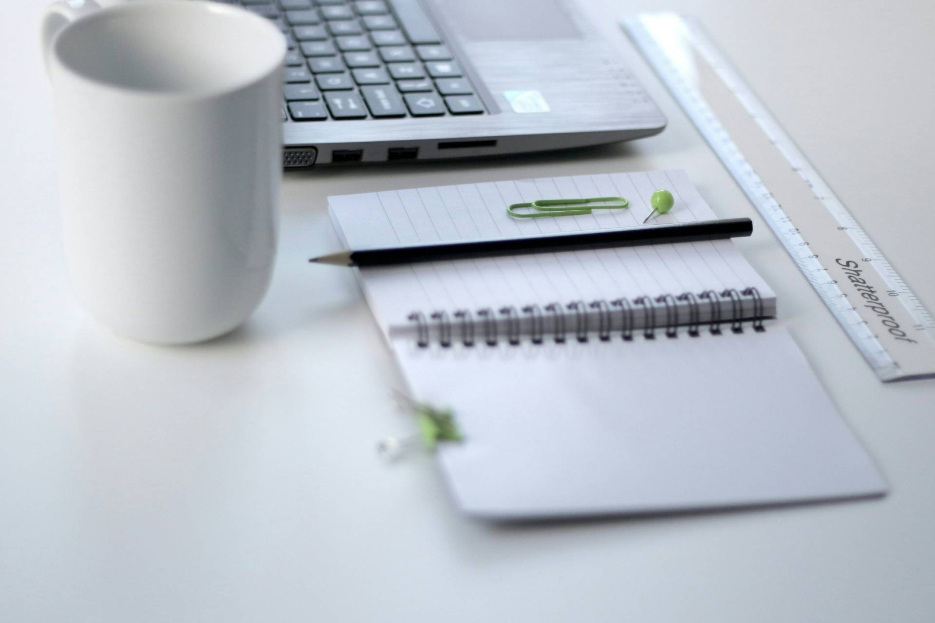 A mug, laptop, notebook, and ruler placed on a white desk