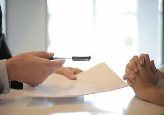 Legal Professional and Client A legal professional passes a document and a pen to a client for signing