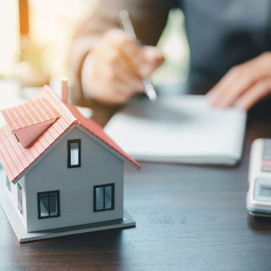 A conveyancer makes notes at his desk. There is a small plastic model of a house placed on the desk.